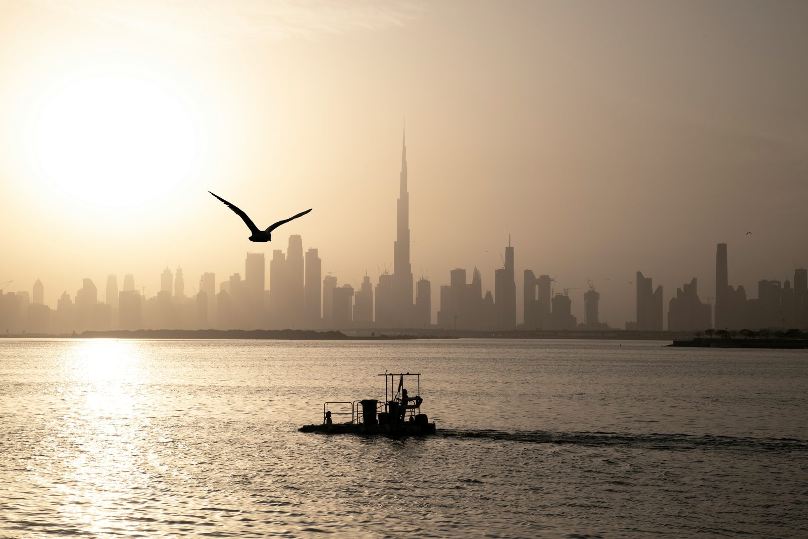 A small boat crossing the water at sunrise, the Dubai skyline in silhouette behind it