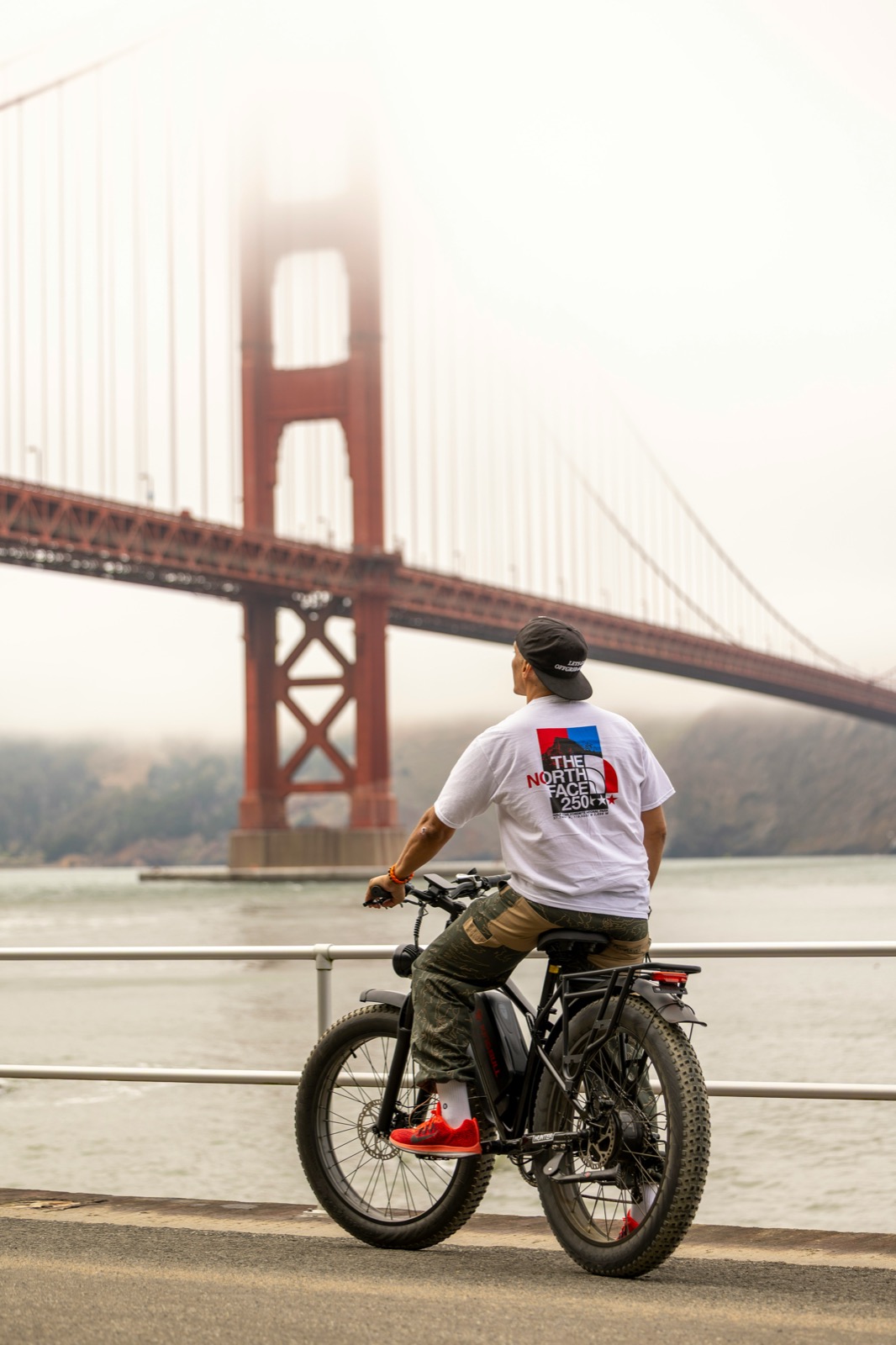 A cyclist pausing on the waterfront path below the Golden Gate Bridge