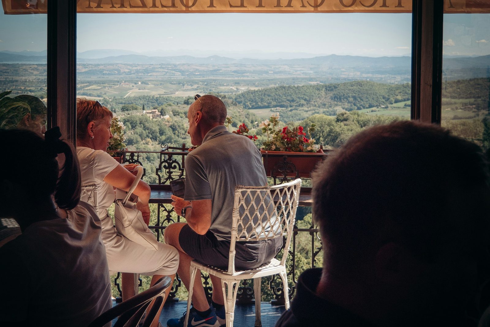 Two people at a hilltop café table, looking out over a wide valley of vineyards