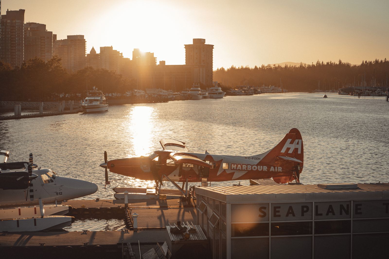A Harbour Air seaplane on the dock at Vancouver's Coal Harbour, downtown towers behind it at sunset